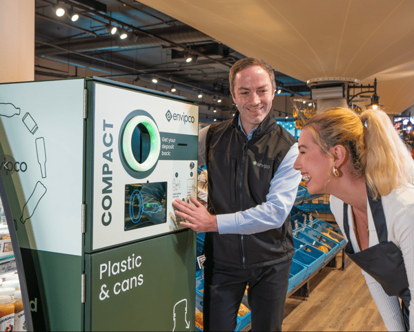 Grocery store staff inspecting an "Envipco Compact" reverse vending machine