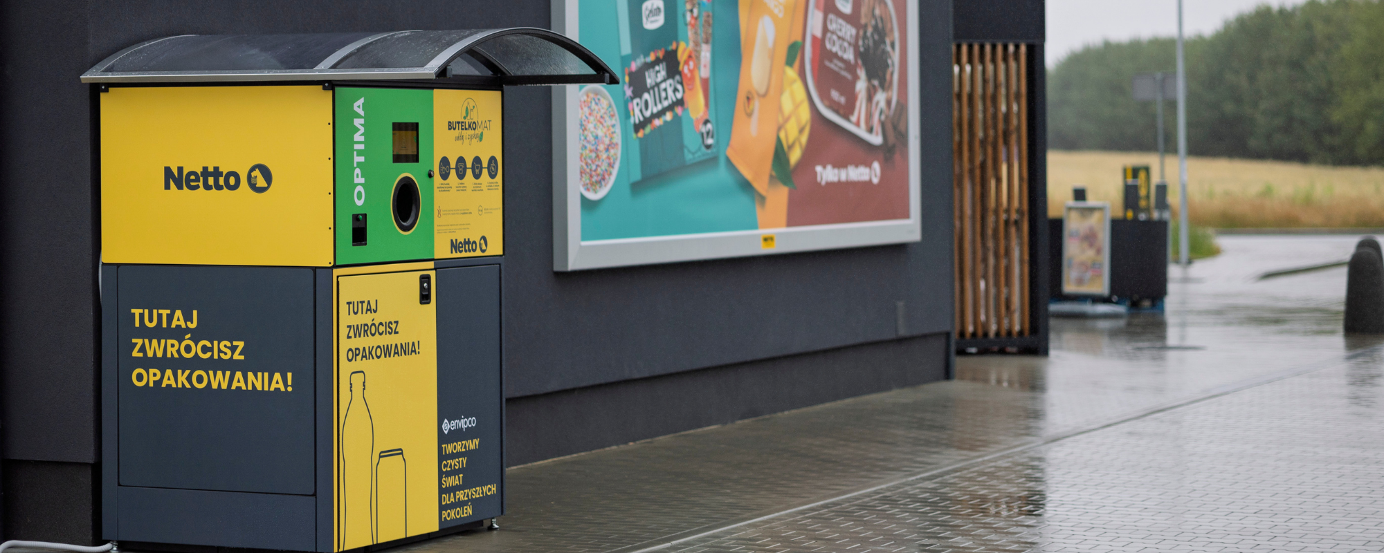 Envipco Optima reverse vending machine with a protective weather canopy standing outside in the rain