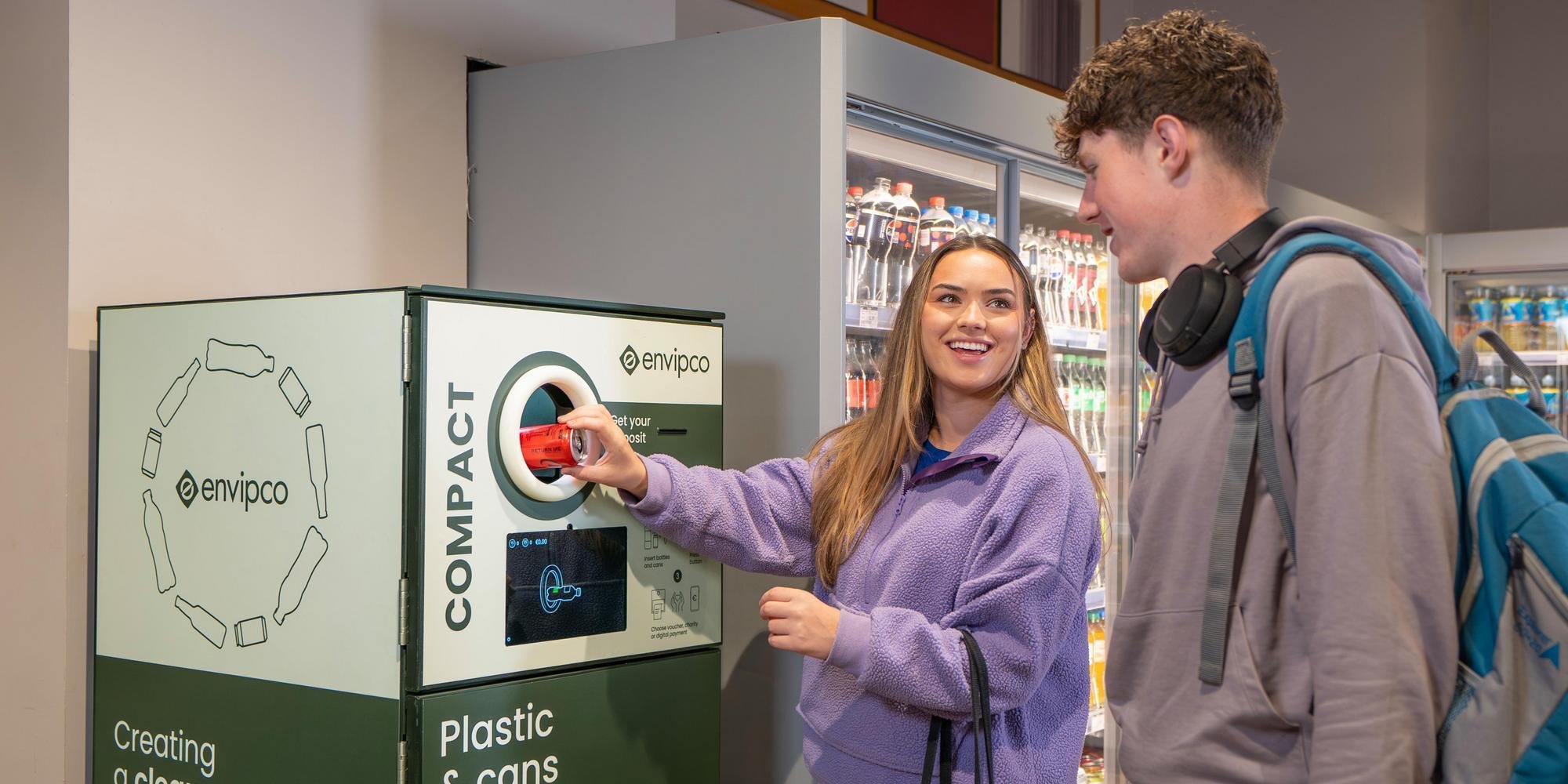 Un consumidor introduce una botella de plástico en una máquina de devolución de envases en un supermercado. Envipco Compact
